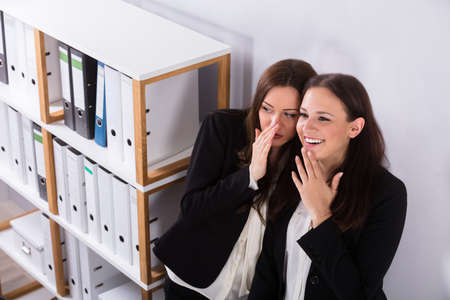 Young Businesswoman Whispering Into Female Colleague's Earの写真素材