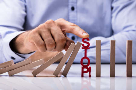 Human's Finger Over Risk Word Stopping Dominos From Falling On Desk