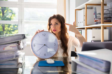 Young Businesswoman With Clock Making Shooting Gesture At Workplaceの写真素材
