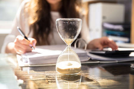 Close-up Of A Hourglass In Front Of Businesswoman Working In Office