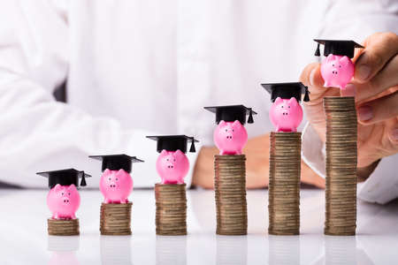 Close-up Of A Person's Hand Placing Piggybank With Graduation Hat On Stacked Coinsの写真素材