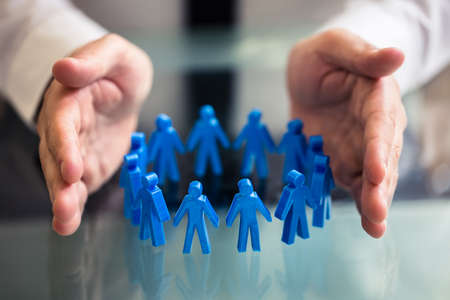 Close-up Of A Businessperson's Hand Protecting Blue Human Figures Forming Circleの写真素材