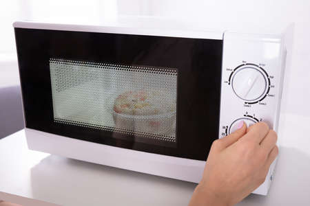 Close-up Of A Woman's Hand Using Microwave Oven For Preparing Foodの写真素材