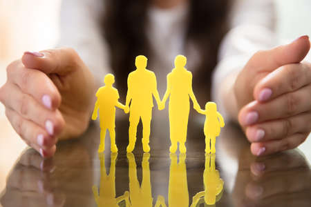 Businesswoman's Hand Protecting Yellow Family Figures Over Desk