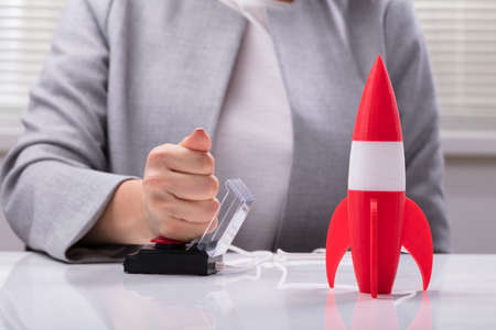 Businesswoman's Hand Launching Rocket By Pressing Red Buttonの写真素材