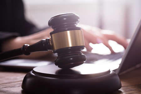 Close-up Of A Gavel On Sounding Block In Front Of Judge Using Laptop