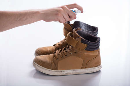 Man's Hand Spreading Deodorant On Smelly Shoes Against White Background