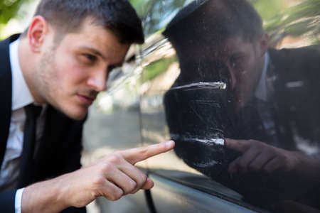 Young Man Inspecting Damaged Car After Accidentの写真素材