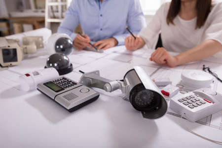 Various Security Equipments In Front Of Two Architects Planning Project On Blueprintの写真素材