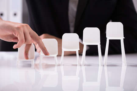 Businessperson Walking On Increasing Size Of Chairs With Finger Over Reflective Background