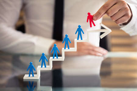 Businessperson Picking Red Human Figure From Staircase Made Of Arrow