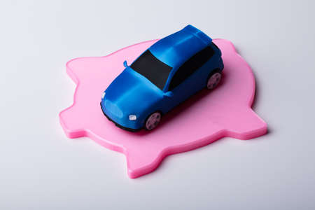 Small Blue Car Over Flat Pink Piggybank Isolated On White Background