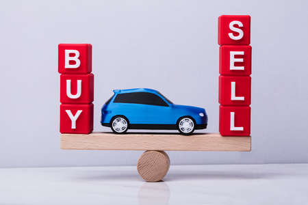 Blue Car Between And Buy And Sell Cubic Blocks Balancing On Wooden Seesaw