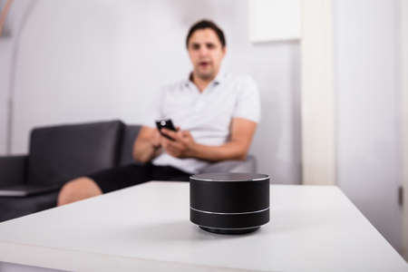 Man with laptop listening to music on wireless speaker at home