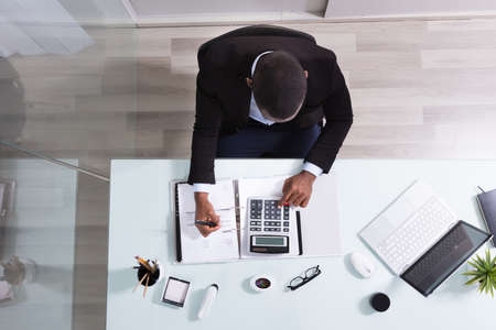 Happy African Businessman Looking At Laptop Calculating Invoice In The Officeの写真素材
