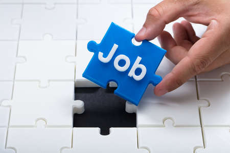 A person's hand placing final blue piece with job word into jigsaw puzzleの写真素材