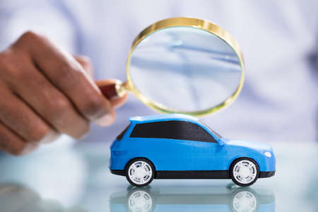 Close-up Of A Person's Hand Holding Magnifying Glass Looking Blue Toy Carの写真素材