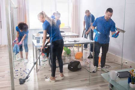 Group Of Young Janitors Cleaning Office With Cleaning Equipment After Partyの写真素材