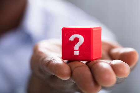 Close-up Of Person's Hand Holding White Question Mark On Red Blockの写真素材