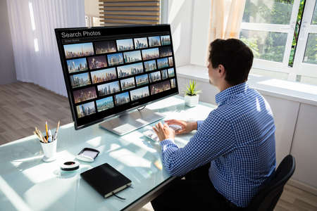Young male editor searching photos on computer in office