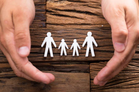 Elevated view of businessperson's hand protecting family figures on wooden backgroundの写真素材