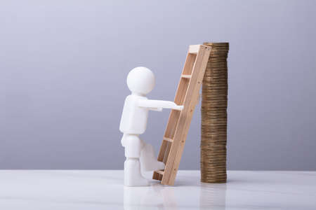 Human Figure Climbing Ladder To Reach On Top Of Stacked Coinsの写真素材