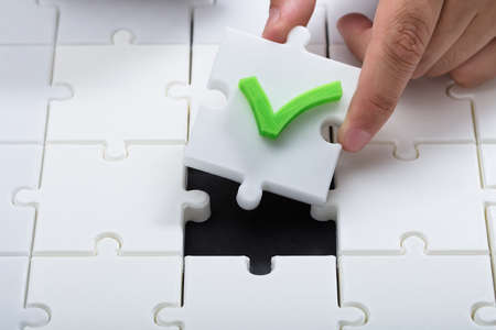 Human hand solving jigsaw puzzle by connecting white piece with check mark