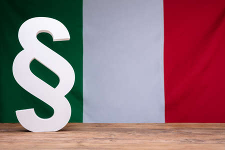 Italian Flag Behind White Paragraph Symbol On Wooden Desk