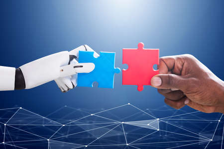 Robot And Human Hand Joining Red And Blue Jigsaw Over The Blue Digital Background Robot And Human Hand Joining Red And Blue Jigsaw Over The Blue Digital Background