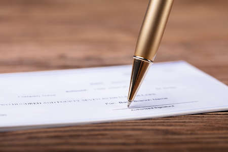 Close-up Of Pen Signing Cheque On Wooden Deskの写真素材