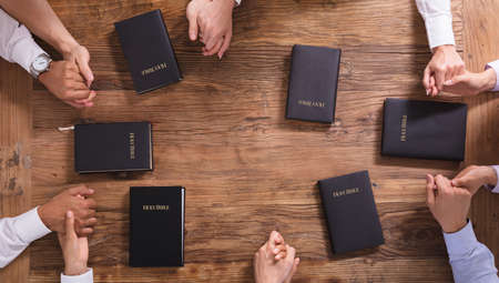 High Angle View Of People's Praying Hands On Holy Bibleの写真素材