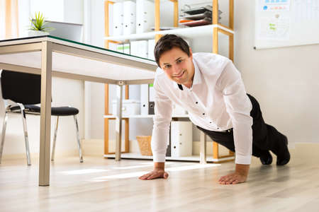 Businessman doing push up on hardwood floor in officeの写真素材