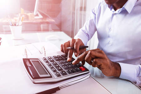 Close-up Of A Businessman Calculating Invoice Using Calculator At Workplaceの写真素材