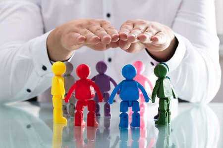 A person's hand protecting multi colored human figures forming circle