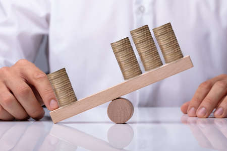 Businessperson's Hand Showing Unbalance Between Stacked Coins On Wooden Seesawの写真素材