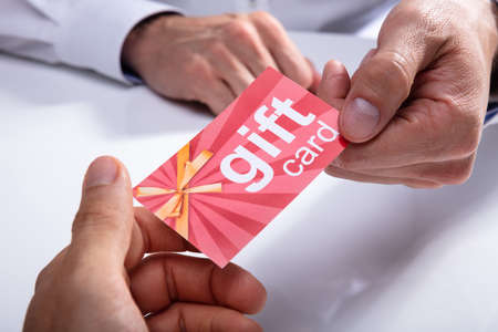Businessman's Hand Giving Gift Card To His Partner Over Desk
