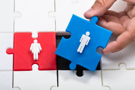 A person's hand placing blue male piece beside red female jigsaw puzzleの写真素材