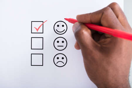 Person's Hand Ticking Off Checked Box Near The Smile Emoji With Red Penの写真素材