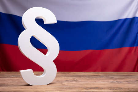 Close-up Of White Paragraph Symbol On Wooden Desk In Front Of Russian Flag