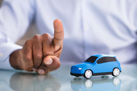 Close-up Of A Businessman Pointing Finger With Blue Toy Car On The Deskの写真素材