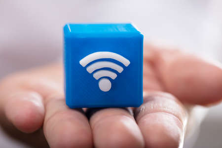 Close-up of a person's hand holding blue cubic block with wireless iconの写真素材