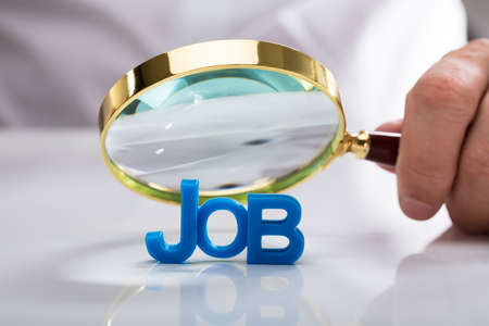 Businessman's hand holding magnifying glass over blue job wordの写真素材