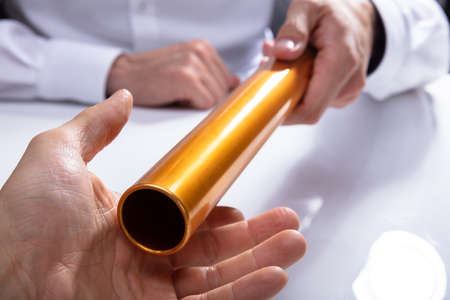 Businessman's Hand Passing Golden Relay Baton To His Partnerの写真素材