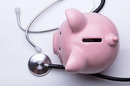 High Angle View Of Pink Piggybank And Stethoscope On White Backgroundの写真素材
