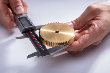 A Person's Hand Measuring Gear's Size With Digital Electronic Vernier Caliper On White Backgroundの写真素材