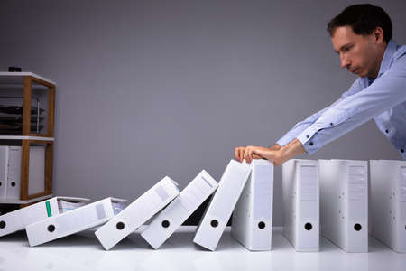 Man Stopping Falling Files On Desk In Officeの写真素材