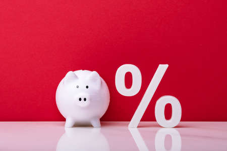 White Piggybank And Percentage Symbol Against Red Wallの写真素材