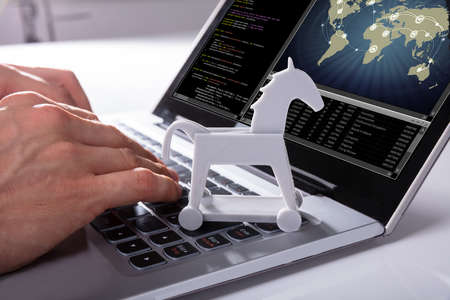 Close-up Of A Hacker's Hand Hacking Global Network With Trojan Horse Icon On Laptop