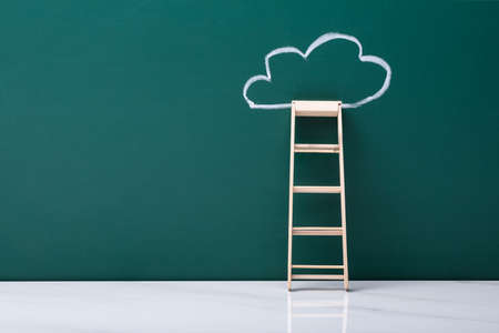 Wooden Ladder Leaning On Green Blackboard With Chalk Drawn Cloudの写真素材