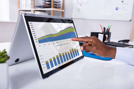 Businessman's Hand Pointing On Laptop Screen Showing Graph Over The Desk